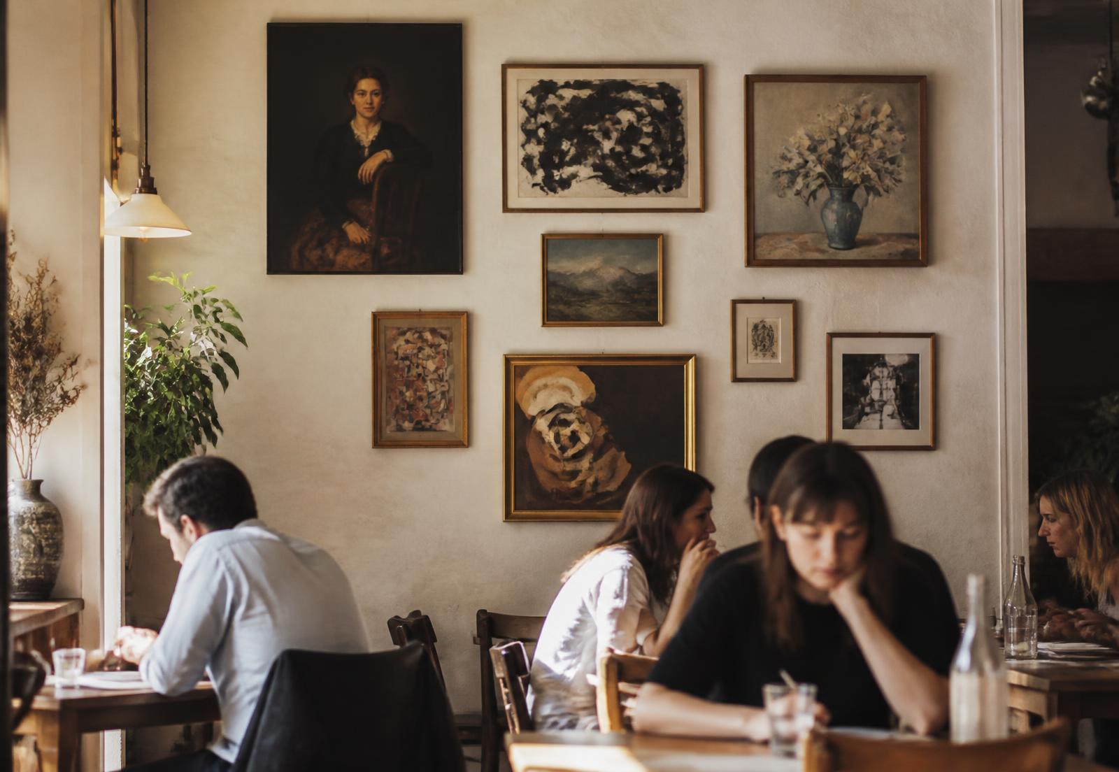 A cafe wall hung with a salon-style cluster of vintage and abstract paintings